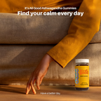 Jar of 'It's All Good' Ashwagandha Gummies on a wooden surface with a person in an orange sweater.