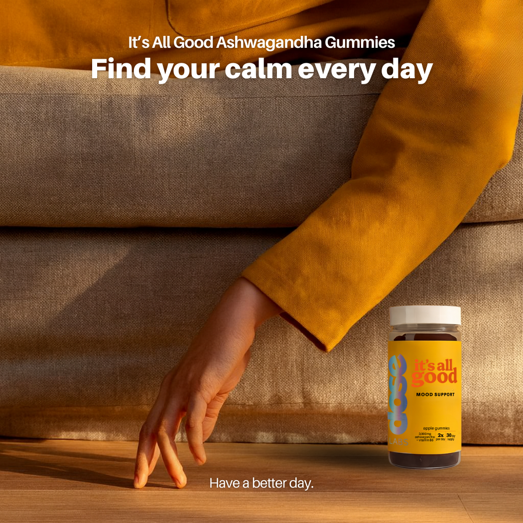 Jar of 'It's All Good' Ashwagandha Gummies on a wooden surface with a person in an orange sweater.