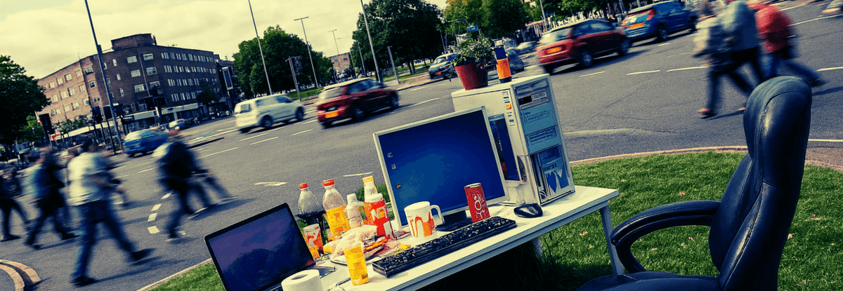 Laptop on a table outdoors with drinks and a city street in the background