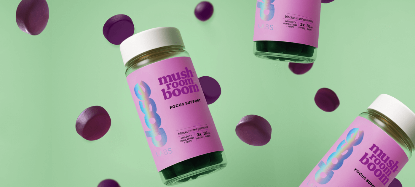 Mushroom Boom product bottles on a green background with purple confetti-like shapes.